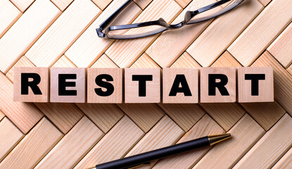 The word RESTART is written on wooden cubes on a wooden background next to a pen and glasses.