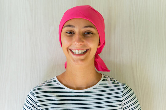 Young delighted female with cancer wearing headscarf standing in apartment and looking at camera