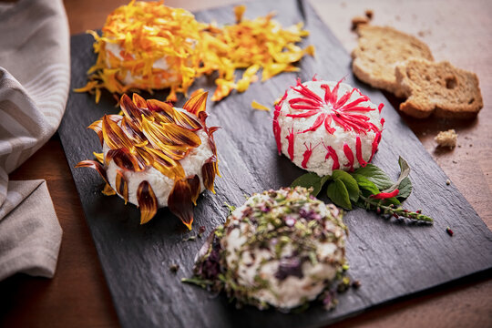 Delicious round shaped curd decorated with edible flower petals and placed on slate board on table in kitchen