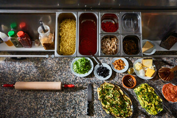 Top view of various fresh ingredients for pizza making on marble table in restaurant kitchen