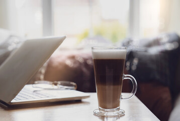 Home made glasses of latte coffee beans and laptop on coffee table in work space  next to window with morning light or Cozy scene of relaxing in afternoon break with coffee and notebook in living room