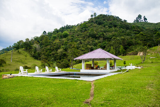Lounge zone of resort with deck chairs at poolside and wooden gazebo on background of grassy hill