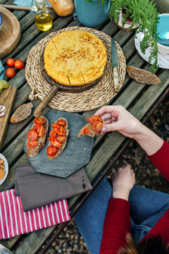 High angle of unrecognizable female friends sitting at wooden table in woods and eating tasty food during picnic in Valle del Jerte in summer