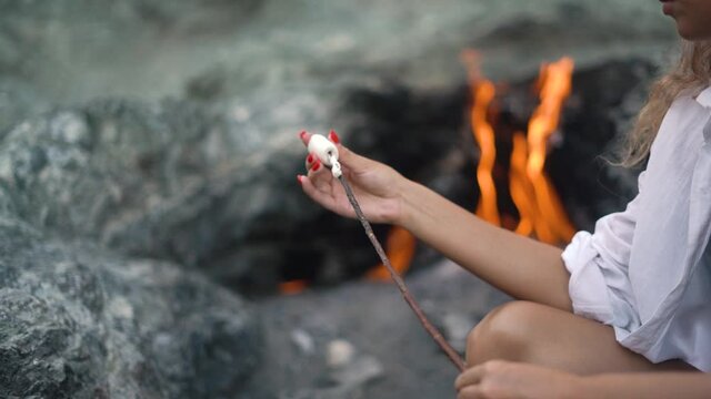 Young lady hands with perfect red manicure string marshmallows on long wooden stick against wonderful natural phenomenon Chimaera mountain fire close view slow motion.