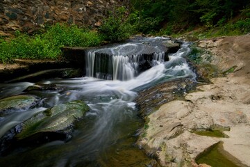 Obraz premium Small waterfall pouring over rocky cascades next to forest