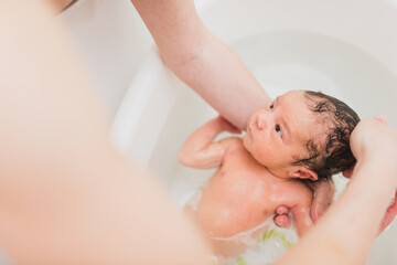 From above unrecognizable parent washing crying newborn baby in warm water in basin at home