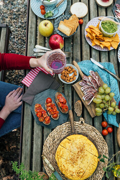 High angle of unrecognizable female friends sitting at wooden table in woods and eating tasty food during picnic in Valle del Jerte in summer