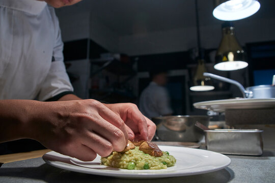 Side view of crop unrecognizable cook assembling pieces of meat on portion of delicious risotto while preparing order in contemporary restaurant kitchen