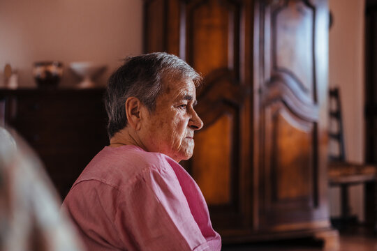 Side view of a senior woman with Alzheimer's mental health issues sitting in a sofa alone in her home