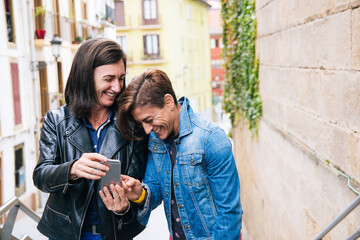 Funny middle aged lesbian couple laughing at something in the mobile phone