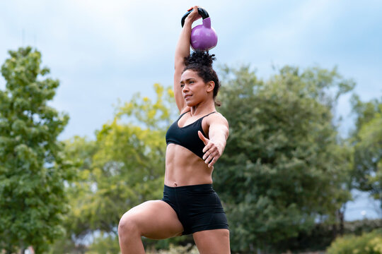 Determined African American muscular sportswoman doing kettlebell snatch exercise during functional workout in park