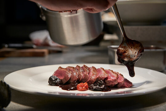 Unrecognizable chef garnishing slices of delicious beef with chocolate sauce while cooking in kitchen of restaurant