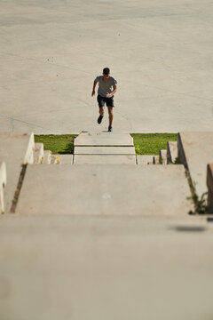 Full body of determined young ethnic sportsman running up stairs during intense fitness workout in sunny summer day