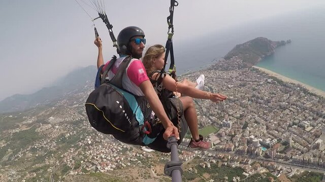 Professional skydiver parachutes lady tourist over small city building silhouettes by yellow sandy beach against endless blue sea in mist on summer day.