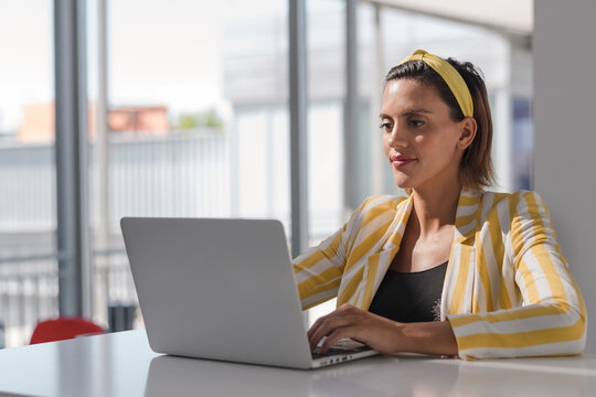 Positive Busy Pregnant Female Remote Worker In Stylish Striped Jacket And Headband Sitting At Table And Browsing Laptop While Working On Project At Home