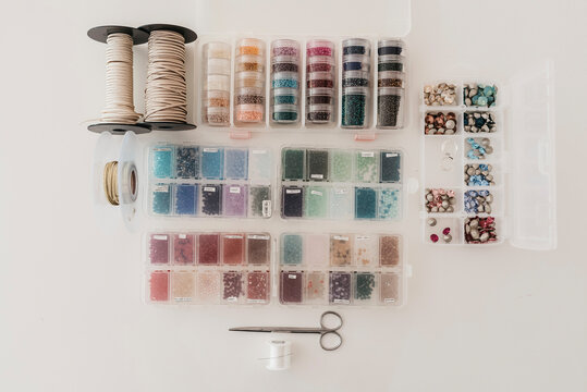 Top view of colorful beads in plastic containers arranged on table with threads and scissors