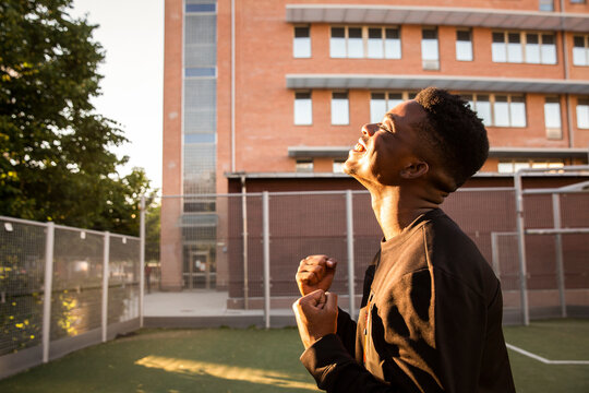 Side view of smiling young man cheering with eyes closed in sports field