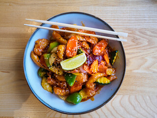 Top view of a pair of chopsticks lying on a bowl with fried vegetables and chicken