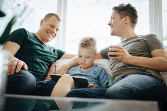 Smiling homosexual fathers talking while son using digital tablet at home