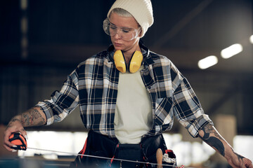 Female carpenter measuring plank with tape