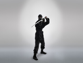 japanese ninja in black uniform with katana sword, on grey background © tankist276