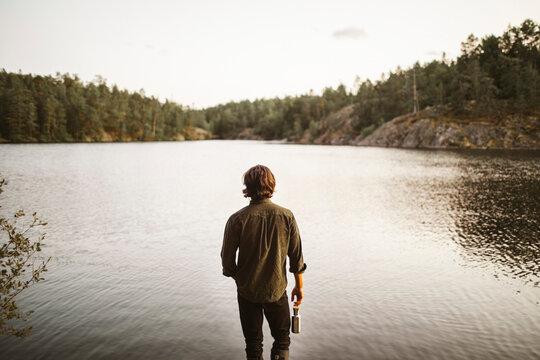 Rear view of man standing by lake in forest during vacation