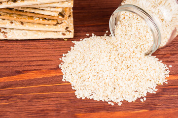 Stack of crispy wheat cakes with sesame seeds, flax and sunflower on a red wooden background and sesame seeds in a jar. zero waste  concept