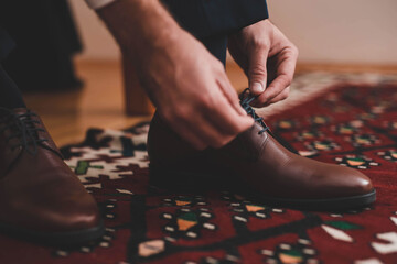 Closeup of a person tying his brown oxford shoelaces with a blurry background