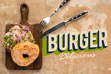 top view of bagel with meat on cutting board with cutlery near burger delicious lettering on textured surface