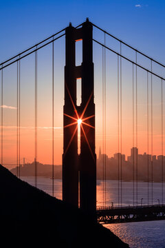 View of Golden Gate Bridge with silhouette of skyline in background during sunrise