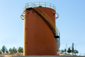 Metal oil storage tank used in oil industry in orange color and clear sky