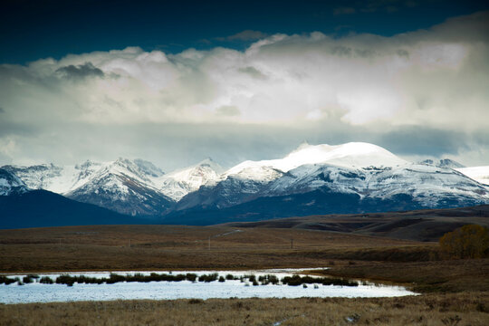 View of small pond in front of snow covered mountain range in Montana