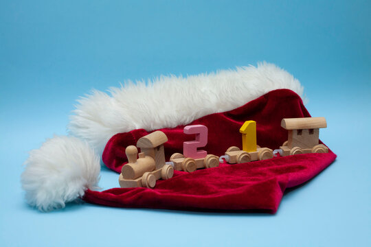 The children's train carries the number 21. The train on a blue background. A children's steam locomotive stands on the hat of Santa Claus. Christmas decorations around the locomotive. Coming 2021