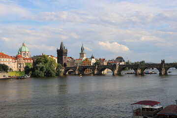 Ancient Charles bridge and the majestic Vltava river in Prague on a hot summer day with clouds