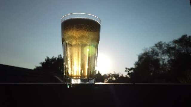 Low medium shot of apple cider being poured into a glass, on a ledge set against the sun and blue sky