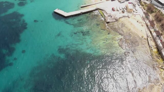 Bird's eye view of Pier extending over Clear Mediterranean water on the shores of Sliema, in Malta - Fly-over aerial shot