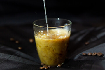 milk is poured into a glass cup with a coffee, on a dark background and sprinkled with coffee beans.