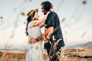 Obraz premium a boy and a girl in love embracing at summer sunset seen through the scrub of a wheat field