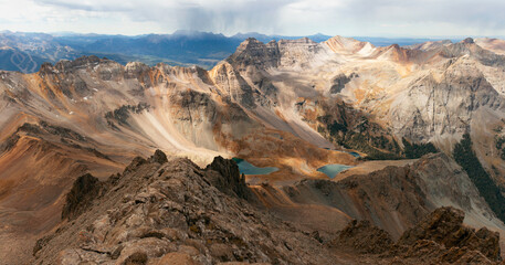 A stunning golden autumn view from the summit of Mount Sneffels of the Blue Lakes and a storm rolling over the distant peaks. Summit views, Blue Lakes, distant storm. 