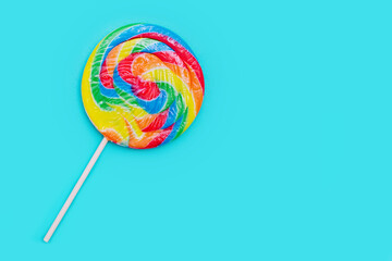 Rainbow lollipop on light blue background. Bright summery food background. Round popsicle. 