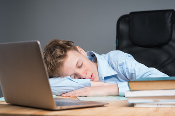 School child in a blue shirt sleeps at a desk with a laptop. Boy fell asleep in class, tired, bored at school. online learning