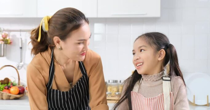 Asian daughter and mom waving hand happily and say hi to camera in kitchen room.