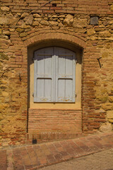 An old partially bricked-in doorway with window shutters in the historic village of Murlo, Siena Province, Tuscany, Italy
