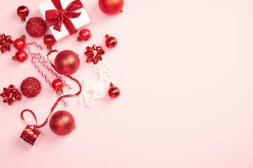 Obraz premium Elegant Christmas composition with gift box and red decoration on pastel pink background. Flat lay, top view. Xmas greeting card design