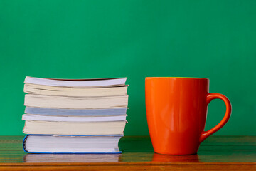 orange mug with stack of books on rustic table and green background