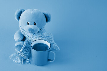 Blue teddy bear with scarf and cup of coffee on blue background. Blue monday concept.