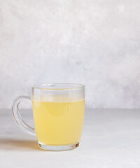 Delicious homemade chicken broth in a glass cup on a light gray background.