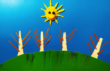 Illustration of the sun with trees on a green hill against a blue sky made of paper strips.