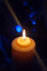 A large candle burns against the background of a garland with shining lights. Vertical photo, defocus. Mystic esoteric romance divination mood christening Christmas carol setcers