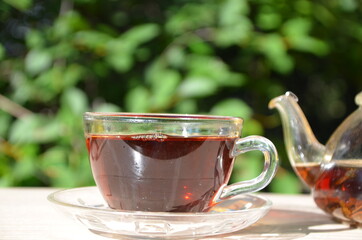 A girl pours tea from a transparent teapot into a transparent cup against a background of green foliage Good morning, outdoor cafe, energy boost. Tea being poured into glass tea